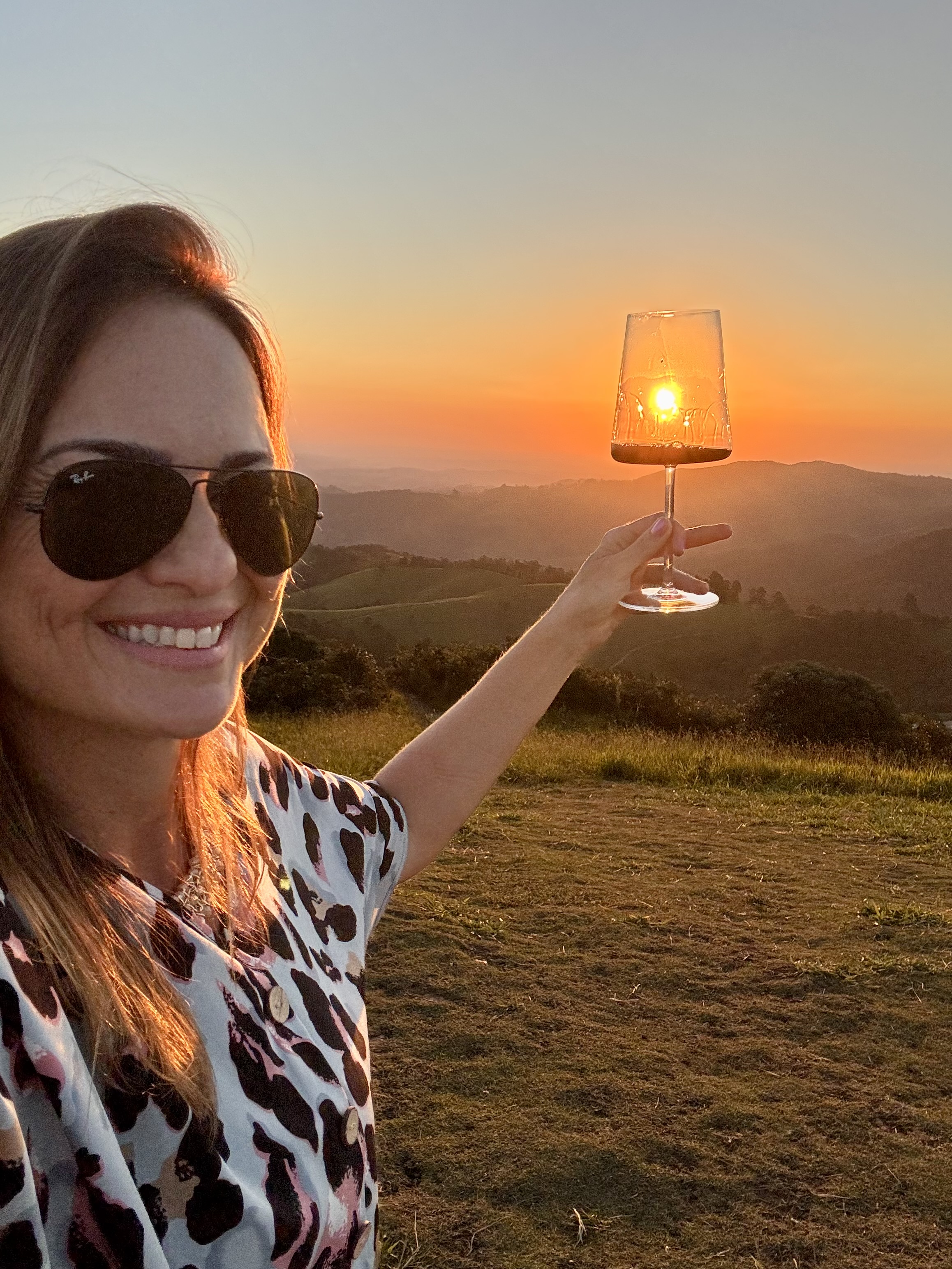 Debora Juneck com taça de vinho ao pôr do sol